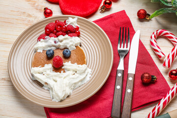 Plate with tasty Santa Claus pancake and Christmas decorations on wooden background