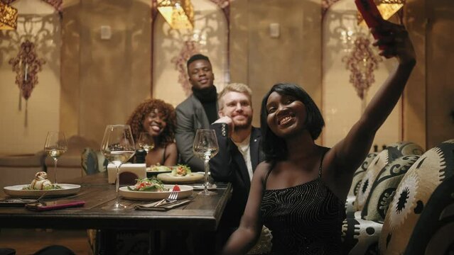 black woman and her multi ethnic friends taking selfie by smartphone in restaurant, happy people