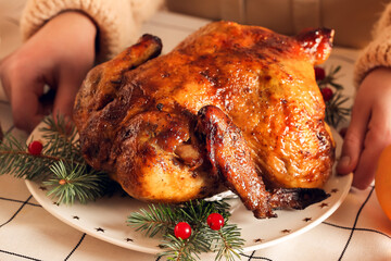 Woman with plate of tasty chicken and Christmas branches on dining table at home, closeup