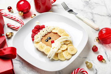 Plate with Santa Claus made of pancake, fruits, whipped cream and Christmas decor on grunge table, closeup