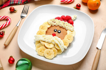 Plate with Santa Claus made of pancake, fruits, whipped cream and Christmas decor on beige table, closeup