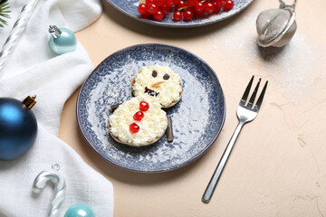 Plate with snowman made of pancakes, whipped cream and Christmas decor on beige table
