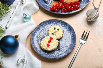 Plate with snowman made of pancakes, whipped cream and Christmas decor on beige table