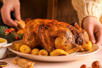 Woman with plate of Christmas chicken and potato on dining table, closeup