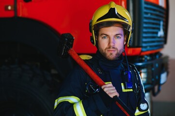 Fototapeta premium Photo of young fireman with sledgehammer in hands near fire engine
