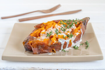 Baked sweet potato Batata served with tahini sauce and fresh thyme on ceramic plate.