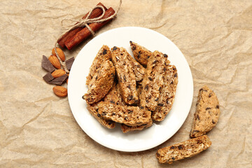 Plate with tasty biscotti cookies, almond nuts, cinnamon and chocolate on beige paper