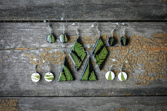 Close up earrings with fern leaves set concept photo. Handmade jewelry. Top view photography with wooden display on background. High quality picture for wallpaper, travel blog, magazine, article