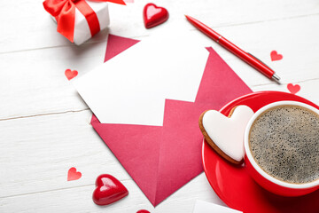 Blank letter with cup of coffee and candies on white wooden background. Valentine's Day celebration