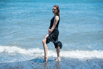 Young woman in black dress walking along the beach.