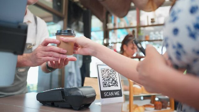 Close up of customer's hand scanning QR code to pay for coffee in cafe.