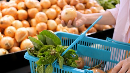 Woman picks up fresh onion in a shopping basket in the vegetable grocery section. The wife buys vegetables from the supermarket to prepare healthy vegetable dishes. Eco-shops with organic vegetables.