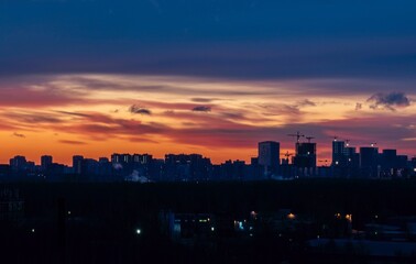 Early richly colorful sunrise over the night city of Moscow. Houses with electric lighting, above the houses there are many construction cranes.