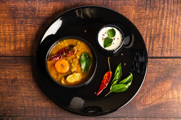 A shot of Sambar and coconut chutney arranged on a black plate on a wooden background. Sambar and chutney are popular in South Indian and Sri Lanka cuisines.