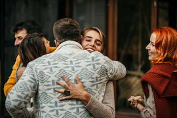 Happy couple welcoming guests at the doorstep of their house who are bringing wine and gifts. The focus is on the man embracing one of the guests.