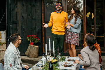 A blindfolded man navigated by his wife is about to be surprised by a group of friends during a garden party.