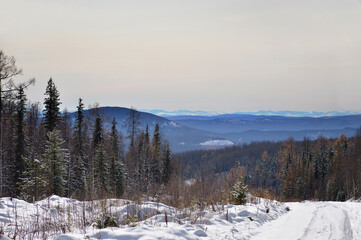 Winter landscape with snow covered forest and mountains. Eastern Sayan Mountains in Siberia, Russia. Road through the pass