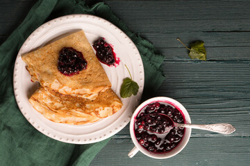 pancakes with blackcurrant jam on a wooden table with a green napkin