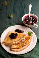 Thin ruddy pancakes with blackcurrant jam on a wooden table with a green napkin