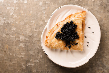 thin pancake with black caviar in a plate