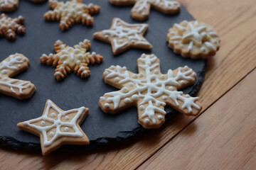 Fototapeta na wymiar Festive gingerbread cookies in shape of Stars and Snowflakes on a black slate stone plate on wooden table