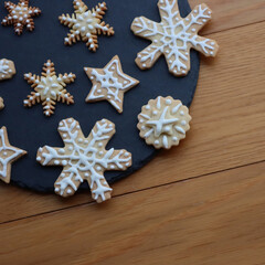 Festive gingerbread cookies in shape of Stars and Snowflakes on a black slate stone plate on wooden table