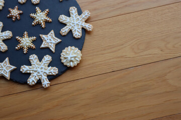 Fototapeta premium Festive gingerbread cookies in shape of Stars and Snowflakes on a black slate stone plate on wooden table
