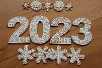 Gingerbread cookies with sugar glaze decoration in the form of numbers 2023 on wooden background. Many Gingerbread cookies in star and snowflake shape. New year concept