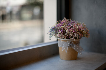 Close-up view of colorful gypsophila flowers in paper pot on windowsill by window
