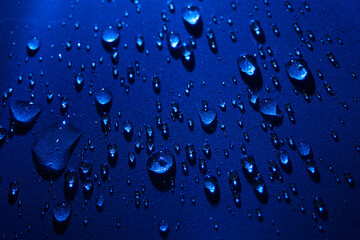 Round drops of water on dark blue background. Through transparent drops of water pass rays of light. View from top. Beautiful back for screensaver. Abstract background..