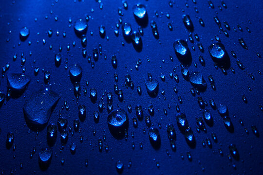 Round drops of water on dark blue background. Through transparent drops of water pass rays of light. View from top. Beautiful back for screensaver. Abstract background..