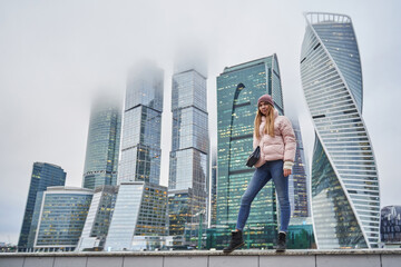 Fototapeta na wymiar beautiful young woman next to skyscrapers and skyscrapers of a big city. tall business centers in the clouds in the background