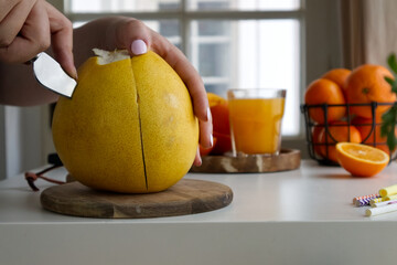  Female hands clean a pomelo standing on a wooden stand and near oranges and juice