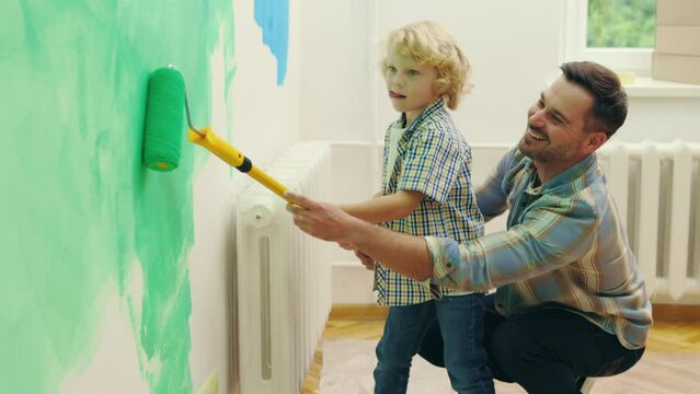 Father and son painting a wall in their home with a roller. Happy child boy helping dad to renovate house. Home repair and family concept