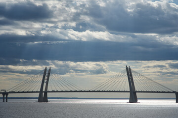 a cable-stayed bridge across the bay and a beautiful sky in the clouds through which the sun breaks through