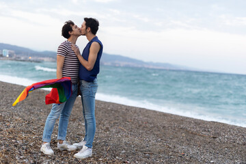 Beautiful gay young couple embraces and holds a rainbow flag. Happy couple enjoy at the beach.