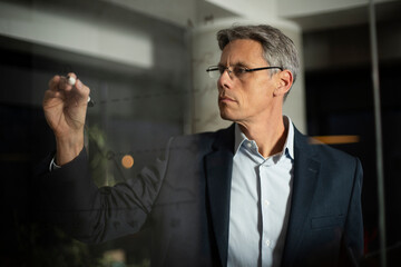 Portrait of successful businessman in office. Man writing on the glass board in office..