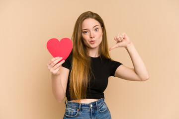 Young redhead woman holding a paper red heart cut out isolated feels proud and self confident, example to follow.