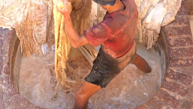 A man washing the leather in a tannery in Fez, with his legs inside the dirty water