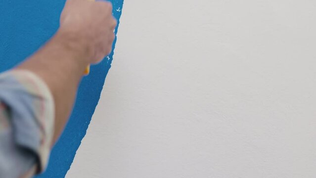 Male worker using roller to paint the walls in the apartment or house in blue color. Roller spreads paint on wall. Close up of the tool.Construction, repair and renovation