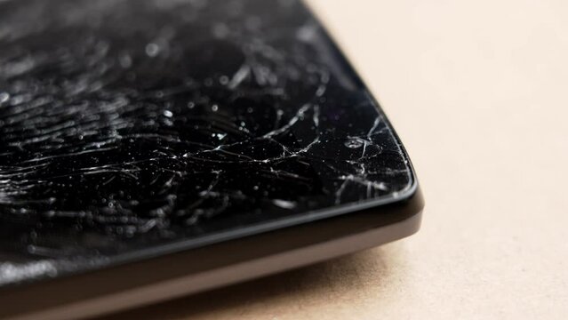 Broken black touchscreen of a mobile phone close-up on a brown surface. Macro. Rotation
