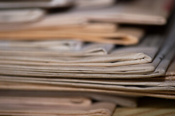 Gros plan sur une pile de vieux journaux. Le bord de certains exemplaires est jauni, la netteté est réalisée sur une petite zone pour voir la texture du papier