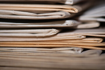 Gros plan sur une pile de vieux journaux. Le bord de certains exemplaires est jauni, la netteté est réalisée sur une petite zone pour voir la texture du papier