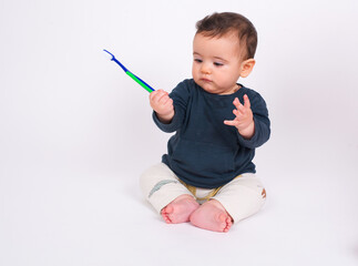 Cute adorable baby boy sitting on white studio background looking at toothbrush and brushing his...
