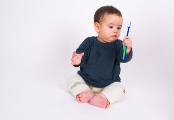 Cute adorable baby boy sitting on white studio background looking at toothbrush and brushing his first teeth.