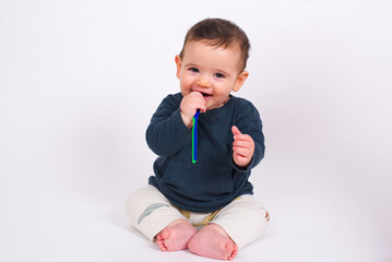 Cute adorable smiling baby boy sitting on white studio background brushing his first teeth.