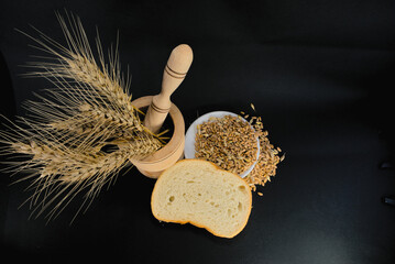 Wheat ears in a wooden mortar and wheat grains in a plate on a black background