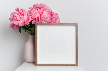 Wooden square frame mockup with pink peony flowers in white room interior