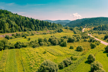 Fototapeta premium Aerial view of the countryside, country road and cultivated fields on the hills on a sunny spring day