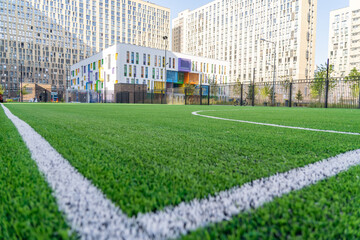 Fototapeta na wymiar Green synthetic artificial grass soccer sports field with white corner stripe line next to modern school building at background